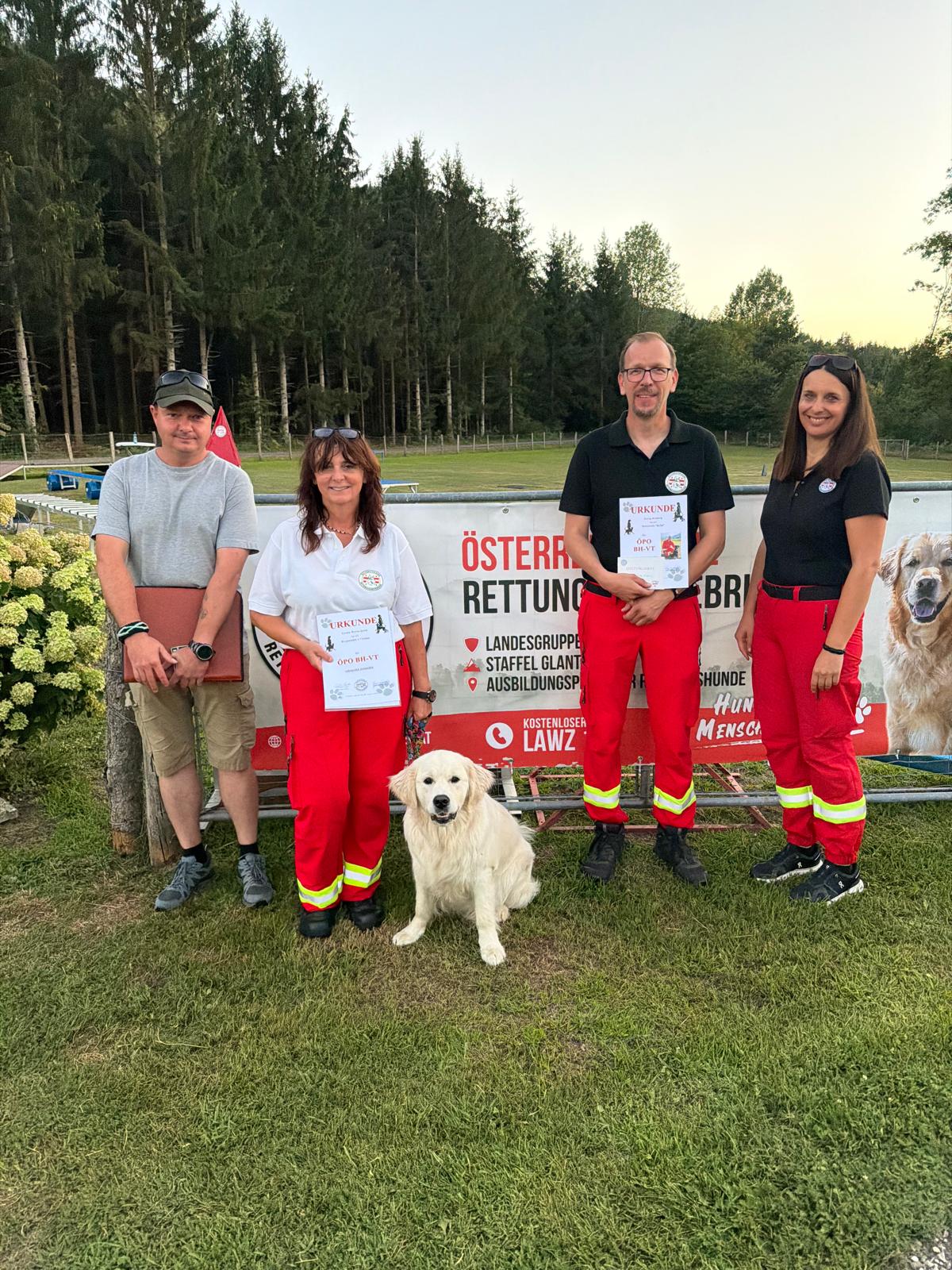 Hunde-Rettungsteam mit Urkunden vor österreichischer Rettungs-Kulisse